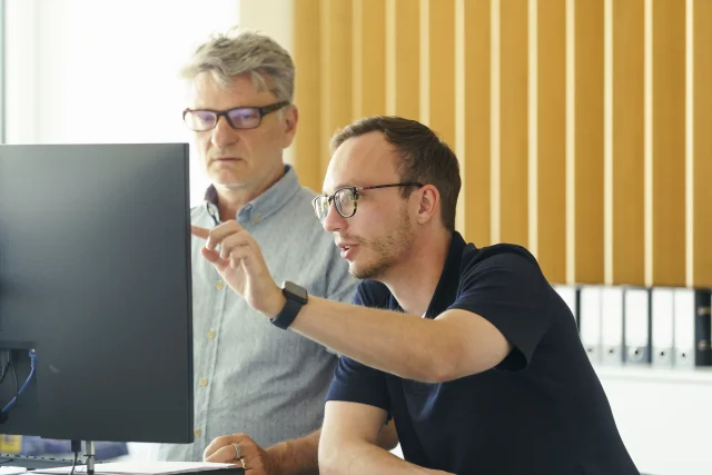 Zwei Männer im Büro schauen auf einen Monitor