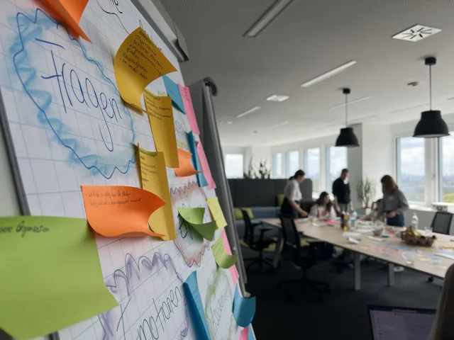 Eine Flipchart mit bunten Zetteln und im Hintergrund Mädchen am Tisch arbeitend