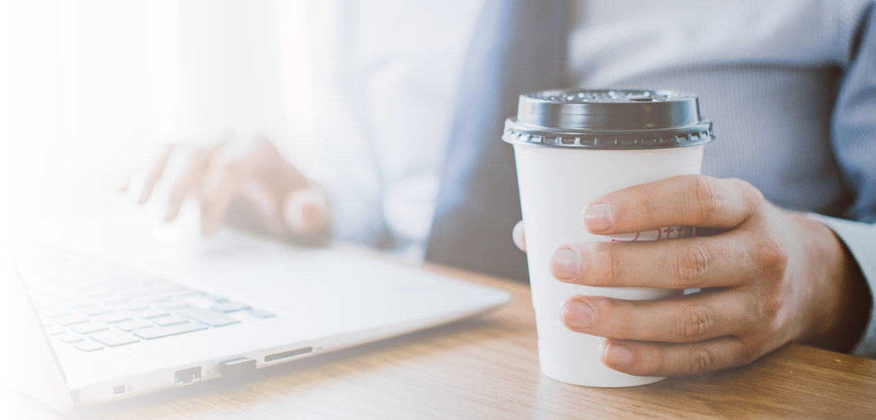 Mann mit Coffee-To-Go-Becher am Laptop